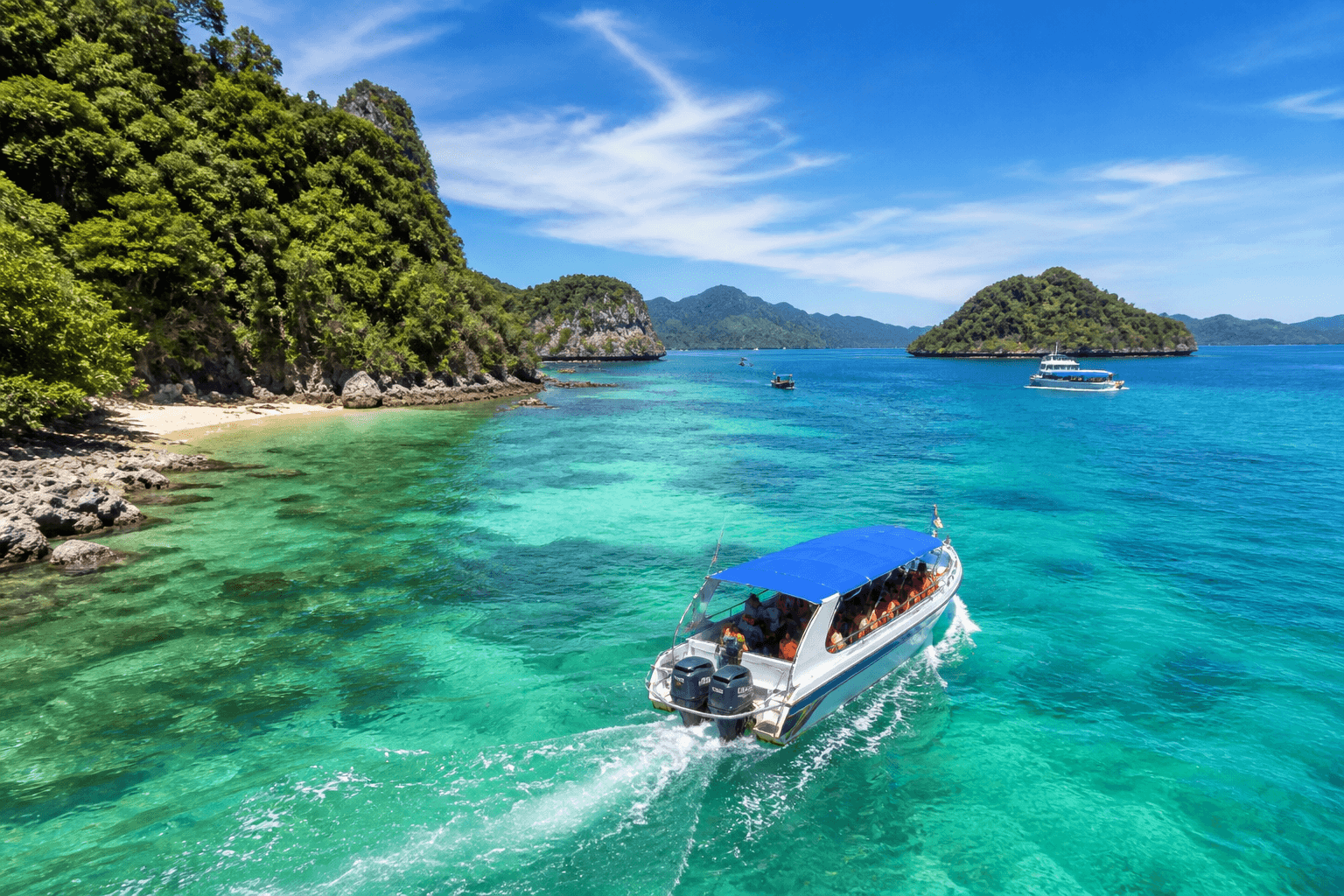 Speedboat cruising through crystal-clear turquoise waters in Langkawi, surrounded by lush green islands and limestone cliffs under a sunny blue sky.